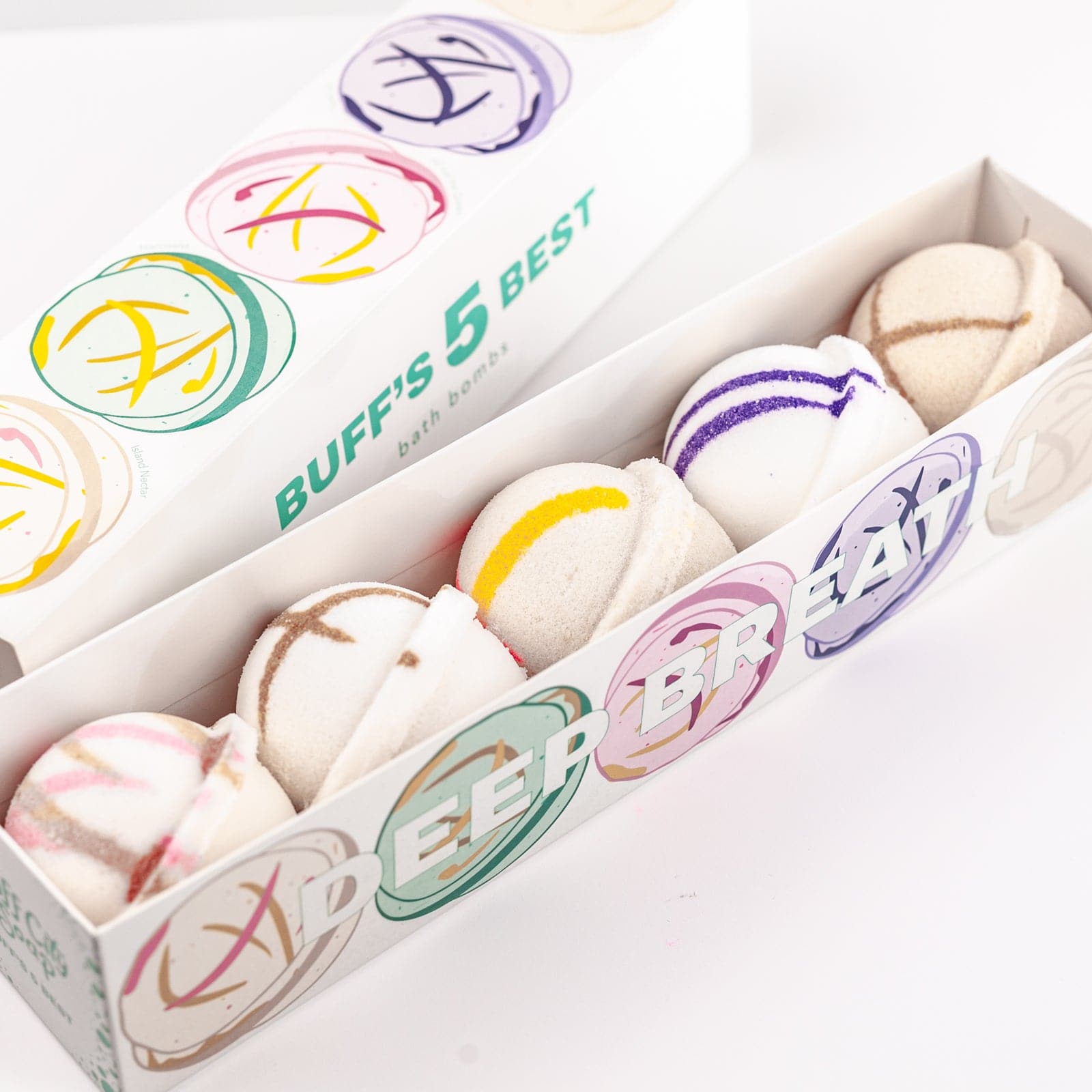 Five Bath Bombs sitting in packaging with varied designs of purple, yellow, brown and pink