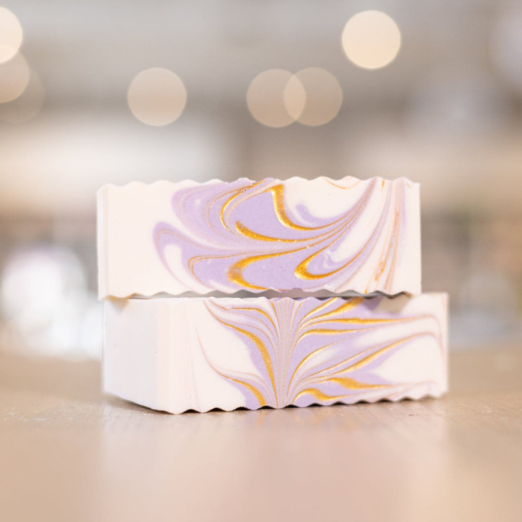 Two white and purple bars of Buff City Soap's lavender shea butter soap stacked on top each other