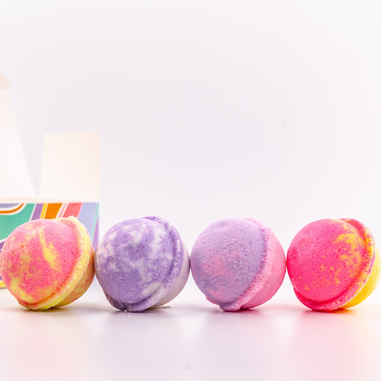 4 multi colored Mini Bath Bombs placed in a row with container in background