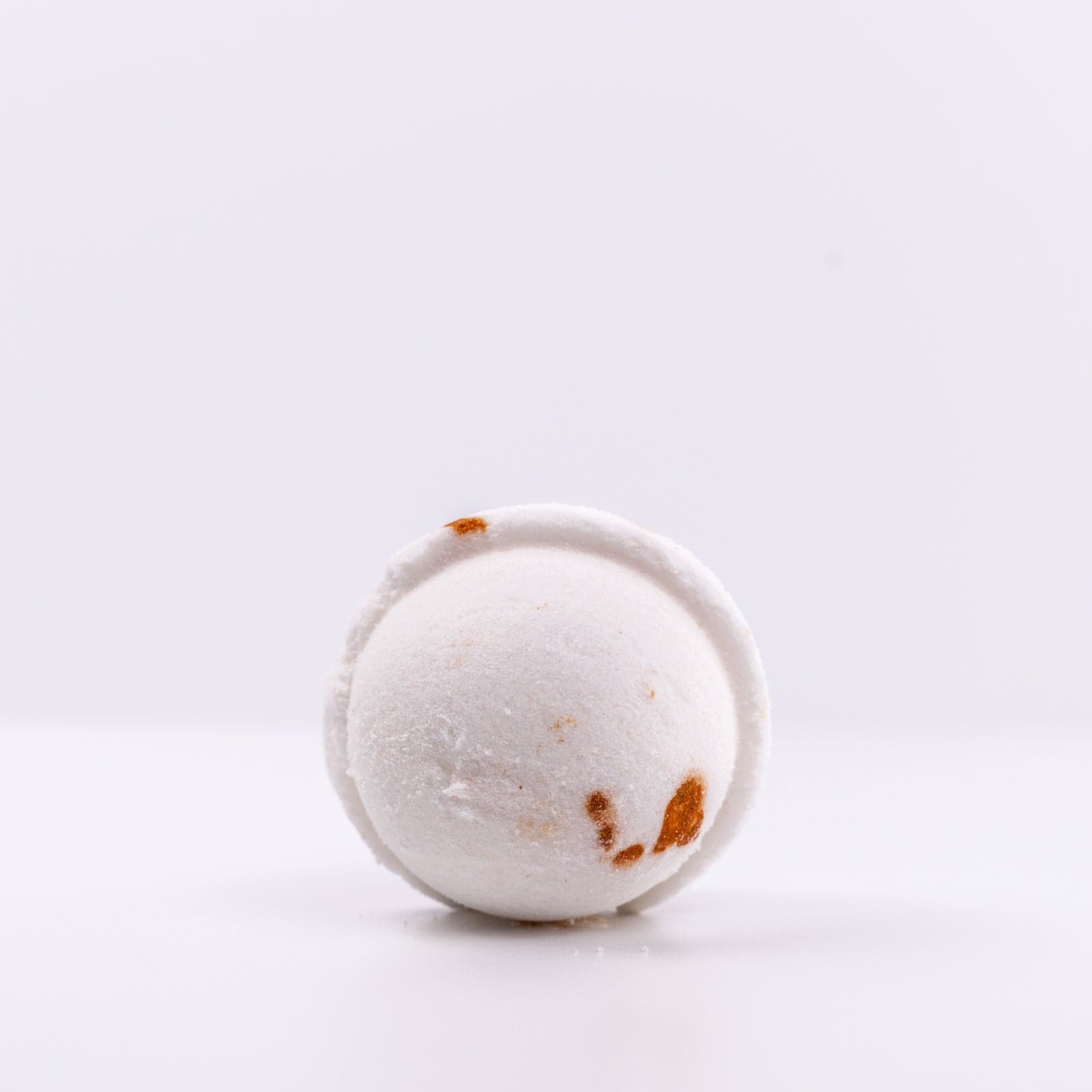 view of the bottom of a white, Narcissist Bath Bomb with dark orange spot